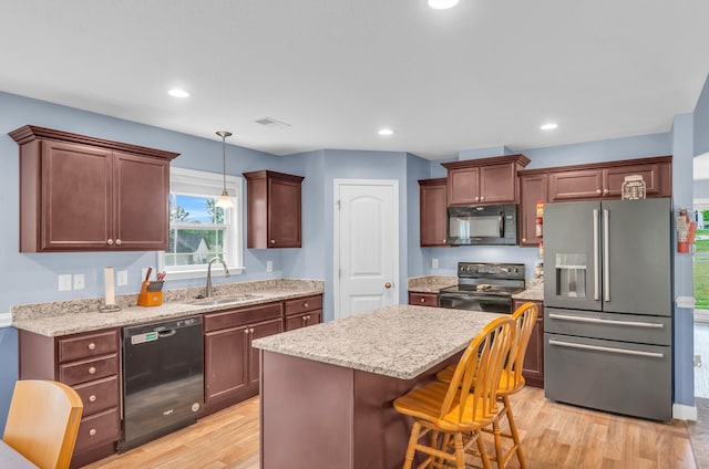 kitchen featuring a sink, light wood finished floors, a kitchen breakfast bar, pendant lighting, and black appliances