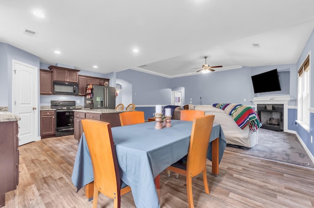 dining area featuring visible vents, a ceiling fan, a fireplace, arched walkways, and light wood-style flooring