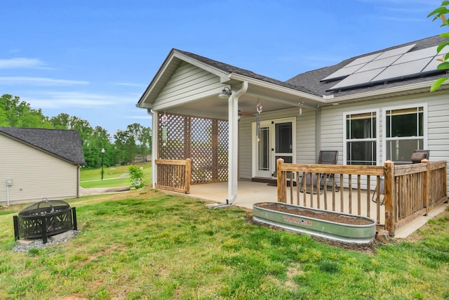 back of property featuring a ceiling fan, roof with shingles, roof mounted solar panels, an outdoor fire pit, and a yard
