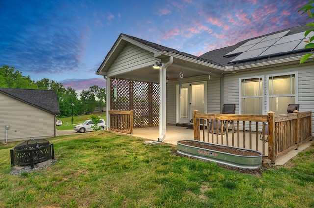 rear view of house with a fire pit, a shingled roof, a patio area, a yard, and solar panels
