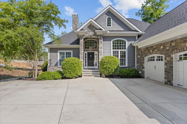 view of front of home with a chimney, a garage, concrete driveway, a shingled roof, and stone siding