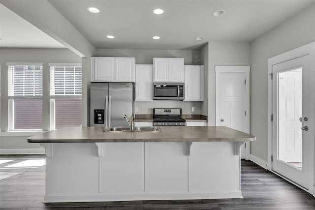 kitchen with an island with sink, a kitchen bar, white cabinetry, a sink, and appliances with stainless steel finishes