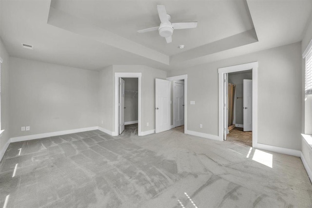 unfurnished bedroom with a walk in closet, a tray ceiling, light colored carpet, and visible vents