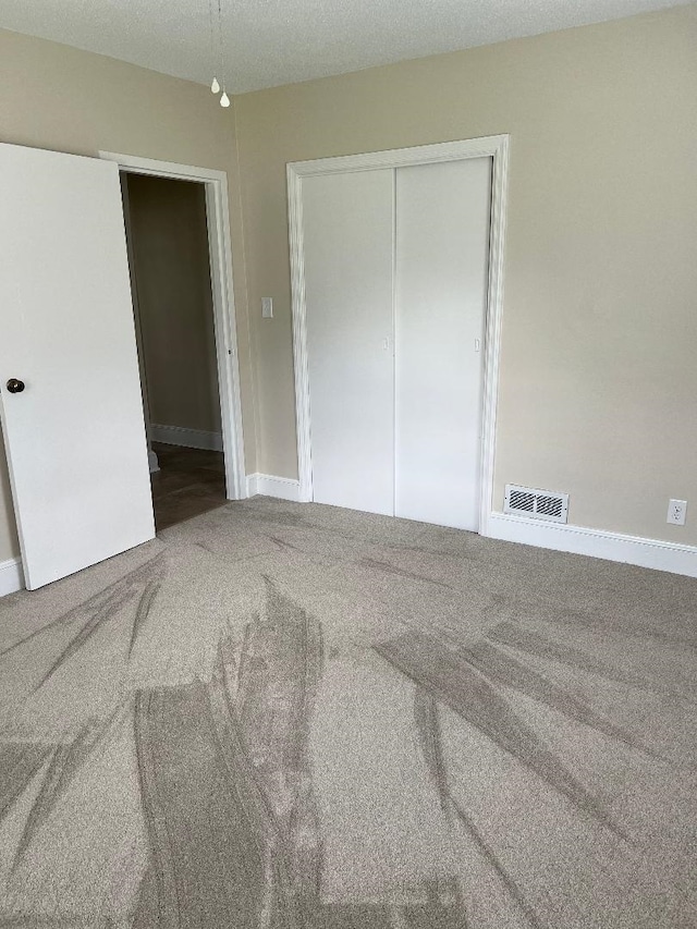 unfurnished bedroom featuring baseboards, visible vents, carpet, and a closet