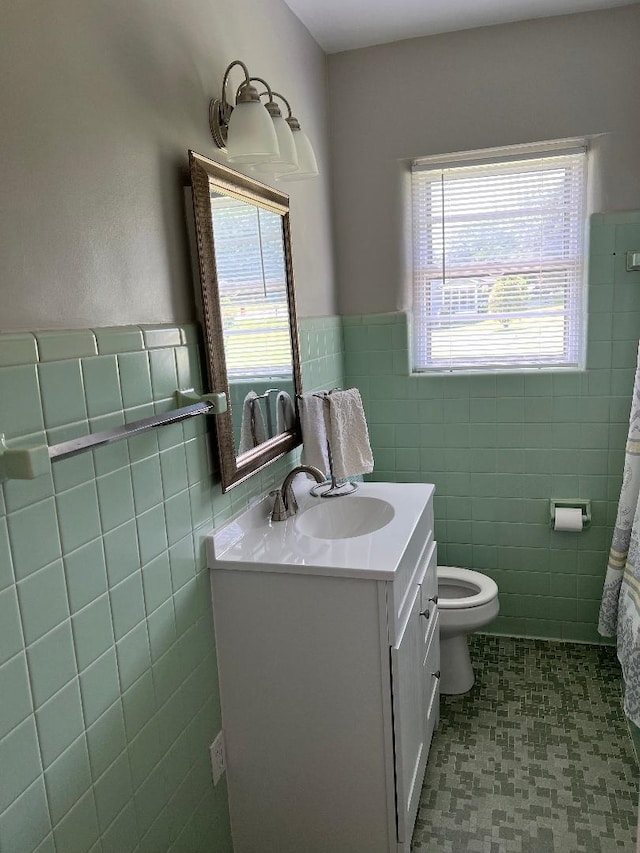 bathroom with toilet, tile walls, wainscoting, and vanity