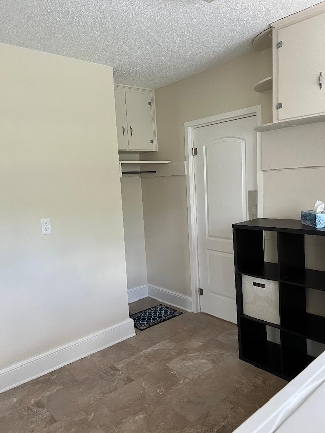 mudroom featuring a textured ceiling, stone finish floor, and baseboards
