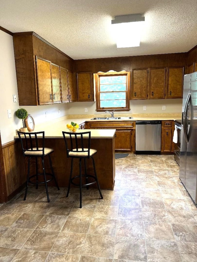 kitchen with a sink, a textured ceiling, appliances with stainless steel finishes, and a peninsula