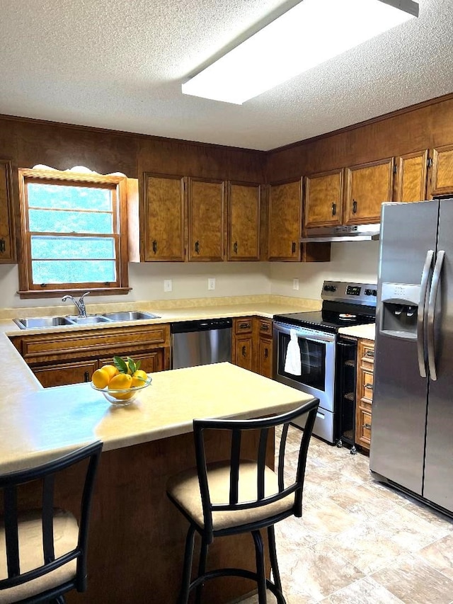 kitchen with a sink, appliances with stainless steel finishes, under cabinet range hood, and a textured ceiling
