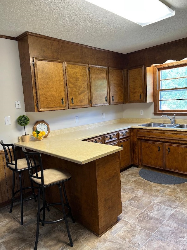 kitchen with a kitchen breakfast bar, a textured ceiling, a sink, light countertops, and a peninsula