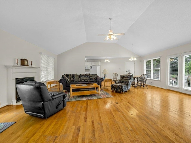 living room featuring lofted ceiling, a fireplace, light wood-style flooring, and ceiling fan with notable chandelier