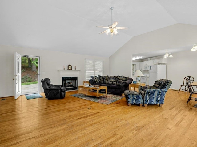 living area with vaulted ceiling, light wood-type flooring, a fireplace, and a ceiling fan