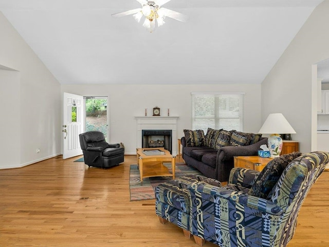 living area with a ceiling fan, light wood-style floors, a fireplace, and vaulted ceiling