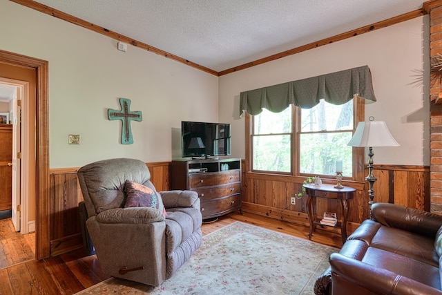 living area with wooden walls, a textured ceiling, hardwood / wood-style floors, and a wainscoted wall