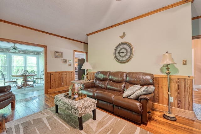 living room featuring wainscoting, ornamental molding, a ceiling fan, and wood walls