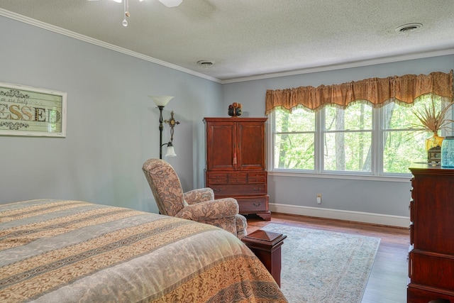 bedroom with wood finished floors, ornamental molding, a textured ceiling, visible vents, and baseboards