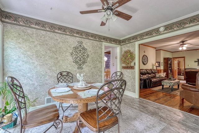 dining area with wood finished floors, wallpapered walls, a textured ceiling, ceiling fan, and ornamental molding