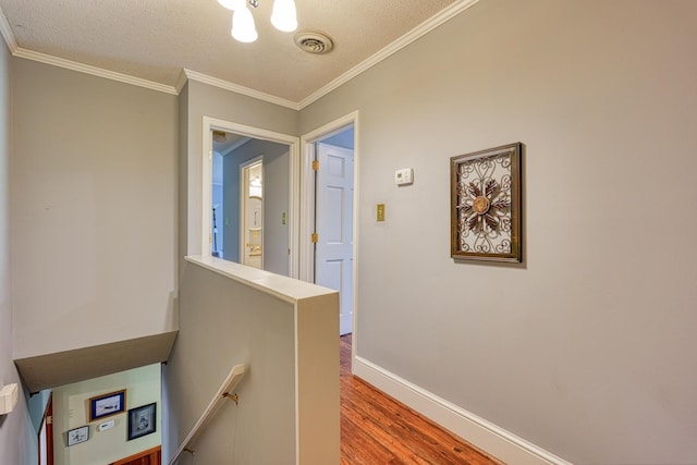 hallway featuring wood finished floors, ornamental molding, a textured ceiling, visible vents, and an upstairs landing