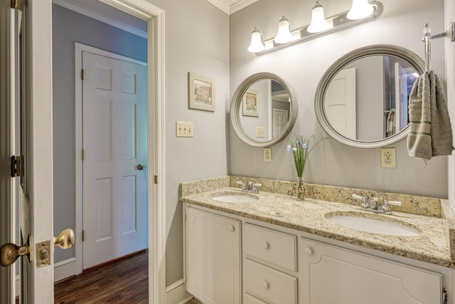full bath with a sink, double vanity, ornamental molding, and wood finished floors