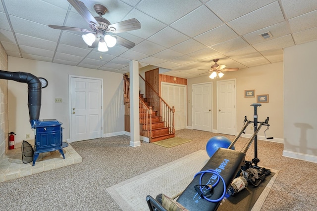 workout area featuring a wood stove, a paneled ceiling, ceiling fan, and carpet floors