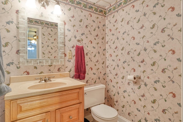 half bath featuring toilet, vanity, and wallpapered walls