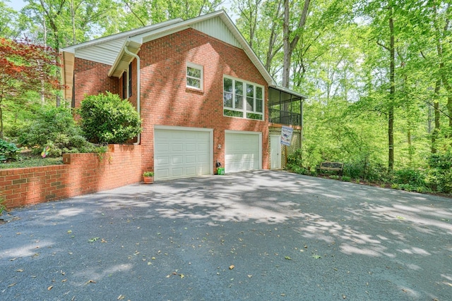 view of side of property with driveway, brick siding, and an attached garage