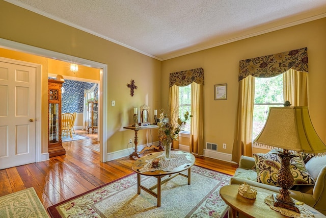 living area featuring hardwood / wood-style flooring, ornamental molding, a textured ceiling, visible vents, and baseboards