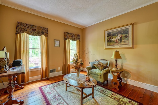 sitting room featuring hardwood / wood-style floors, a textured ceiling, visible vents, baseboards, and ornamental molding