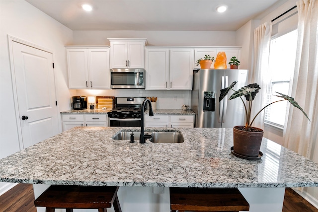 kitchen with a kitchen bar, a sink, white cabinets, a center island with sink, and appliances with stainless steel finishes