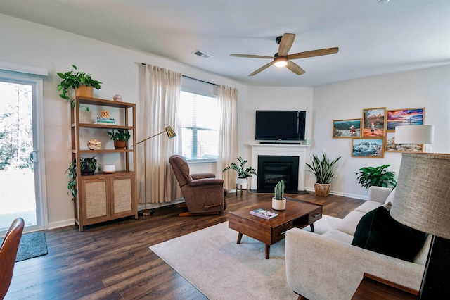 living area featuring visible vents, dark wood-style flooring, a ceiling fan, baseboards, and a fireplace with flush hearth