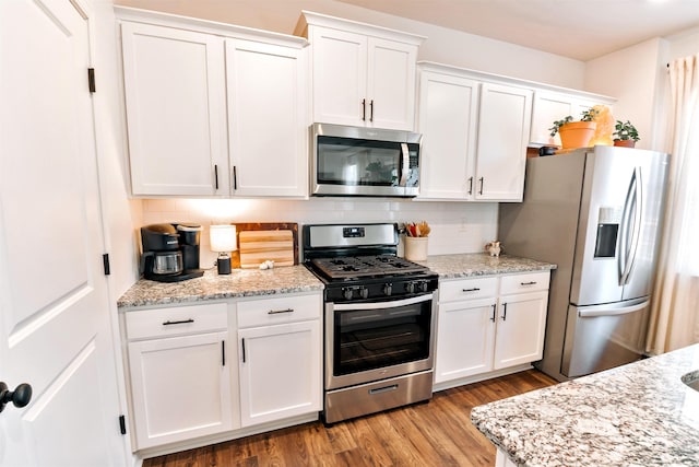 kitchen featuring light stone counters, white cabinets, wood finished floors, tasteful backsplash, and appliances with stainless steel finishes