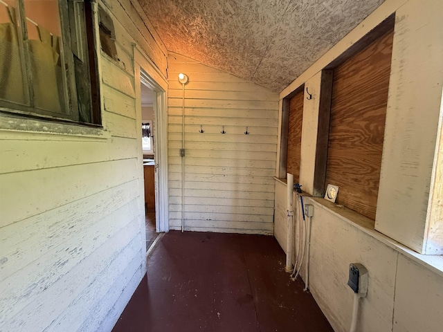 hallway featuring vaulted ceiling and wood walls