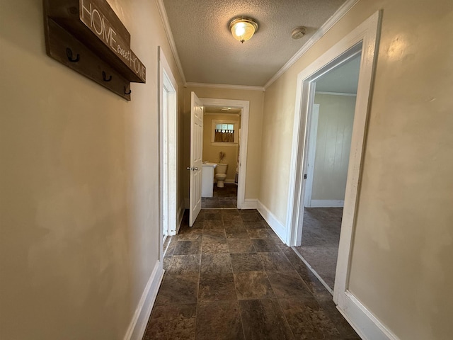 hall featuring ornamental molding, a textured ceiling, baseboards, and stone finish floor
