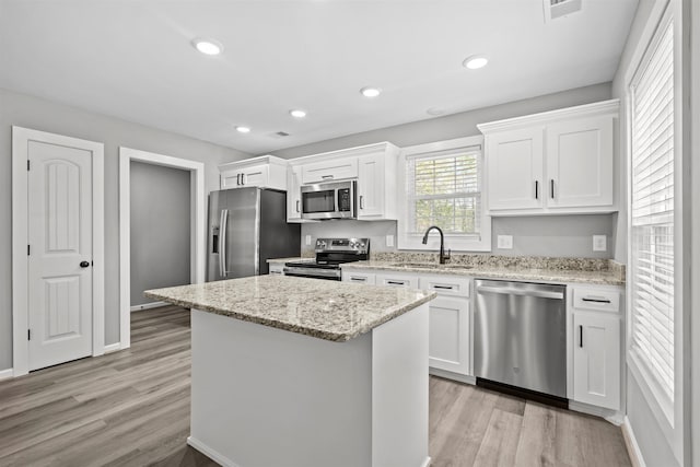kitchen with a sink, appliances with stainless steel finishes, white cabinets, a kitchen island, and light wood-style floors