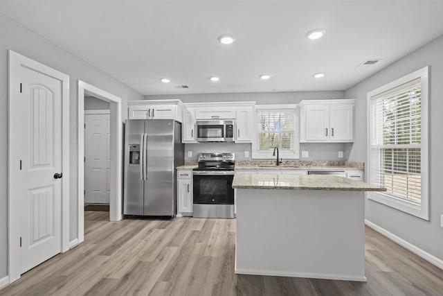 kitchen featuring a sink, stainless steel appliances, white cabinets, plenty of natural light, and light wood-style floors