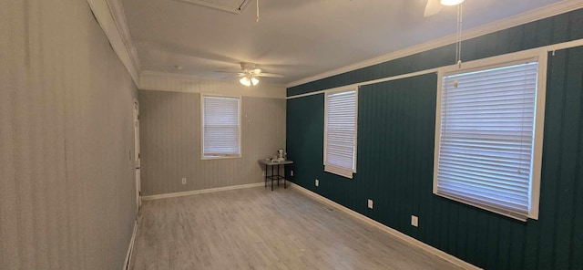 empty room with wood finished floors, attic access, crown molding, baseboards, and ceiling fan