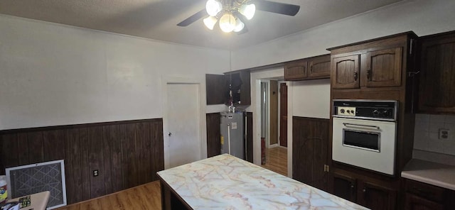 kitchen featuring ceiling fan, dark brown cabinetry, light countertops, water heater, and oven