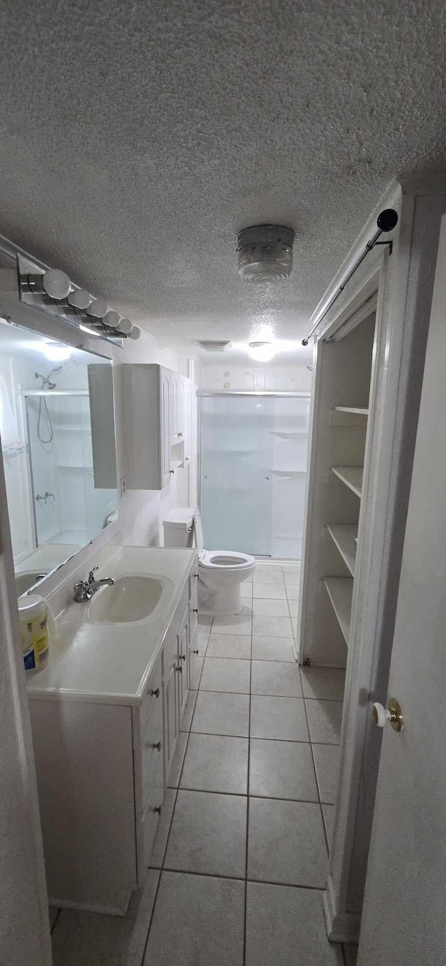 bathroom with walk in shower, toilet, vanity, a textured ceiling, and tile patterned flooring