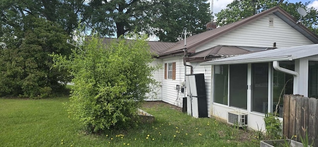 view of side of home featuring a sunroom, cooling unit, a chimney, and a lawn