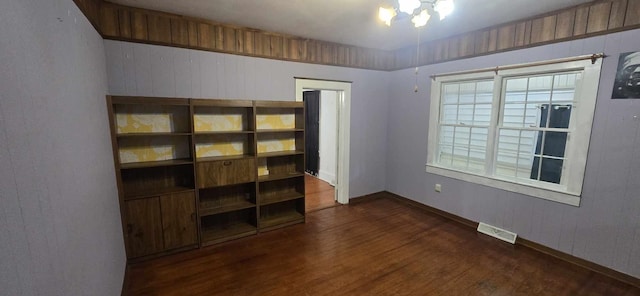 unfurnished room with an inviting chandelier, baseboards, visible vents, and dark wood finished floors