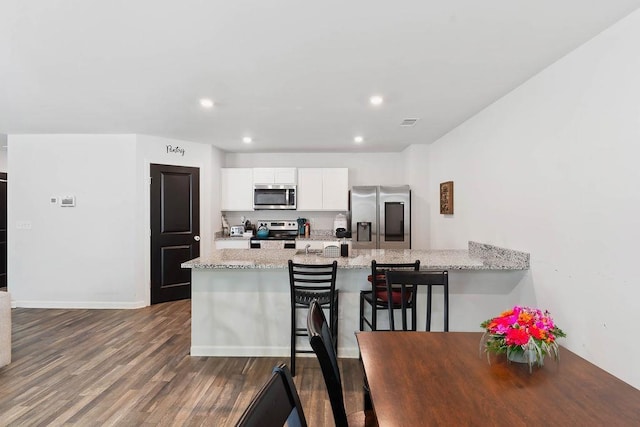 kitchen featuring recessed lighting, light stone counters, a peninsula, stainless steel appliances, and white cabinets