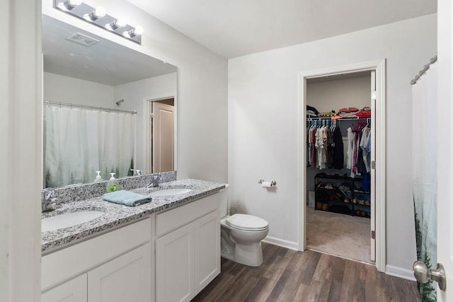 full bathroom with a sink, double vanity, toilet, and wood finished floors