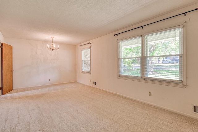 carpeted spare room with a textured ceiling, visible vents, a healthy amount of sunlight, and a notable chandelier