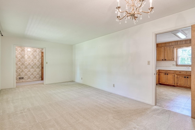 unfurnished living room with a sink, light carpet, a notable chandelier, and baseboards