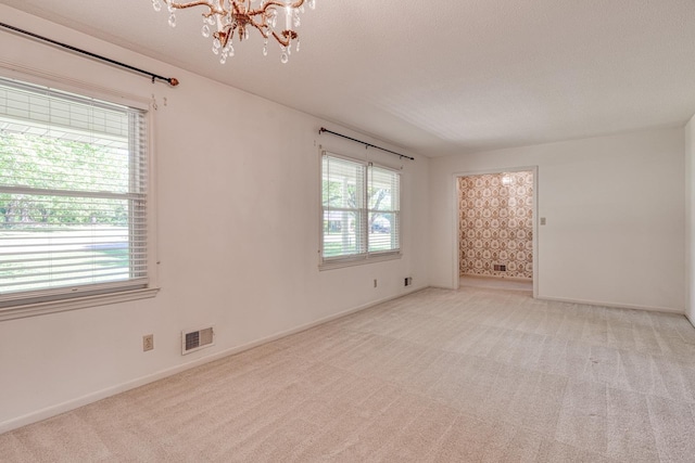 unfurnished room featuring a chandelier, light carpet, plenty of natural light, and visible vents