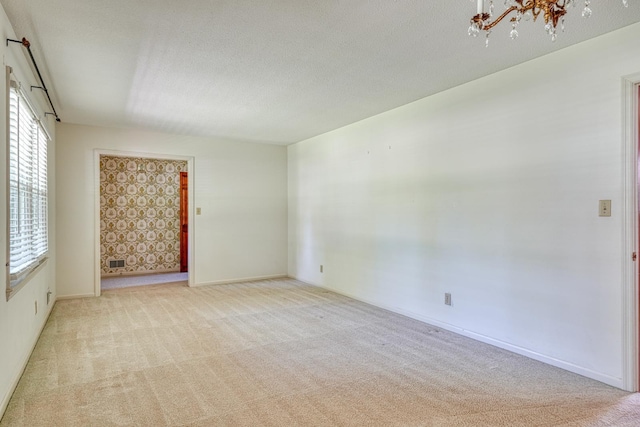 carpeted spare room featuring an inviting chandelier, a textured ceiling, and baseboards