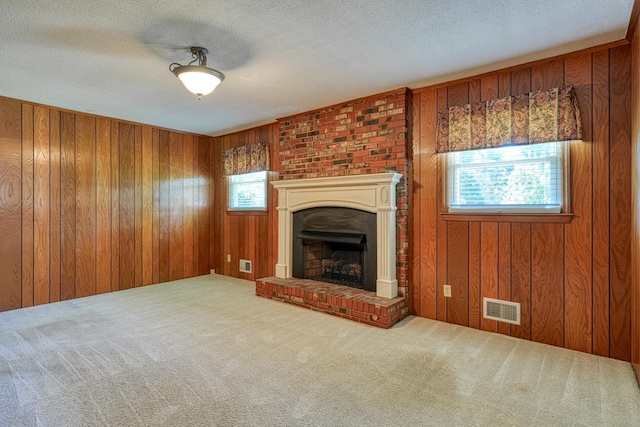 unfurnished living room with wooden walls, a fireplace with raised hearth, visible vents, and carpet