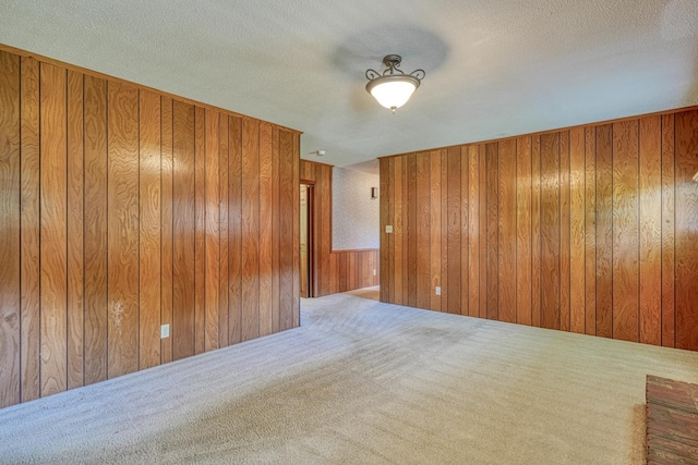 empty room featuring a textured ceiling, wooden walls, and carpet