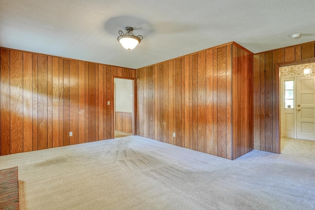 carpeted spare room with a textured ceiling and wooden walls