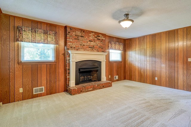 unfurnished living room featuring carpet flooring, visible vents, wood walls, and a fireplace with raised hearth