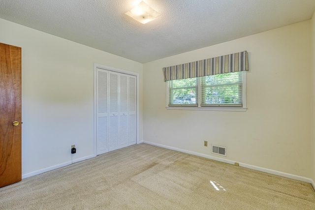 unfurnished bedroom with a closet, a textured ceiling, baseboards, carpet flooring, and visible vents